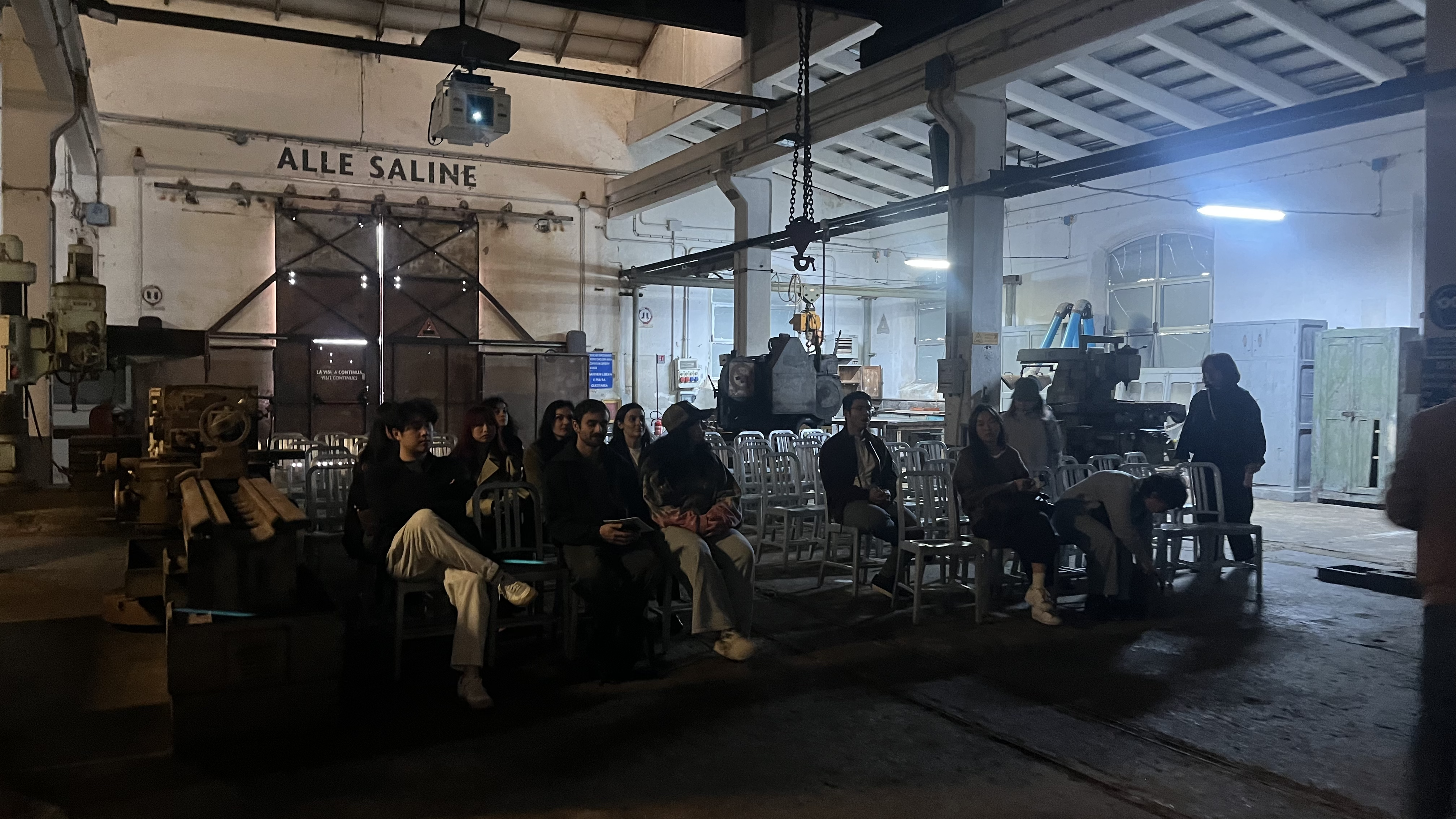 Visitors seated in the foundry space labelled 'Alle Saline', watching a projection surrounded by preserved industrial machinery